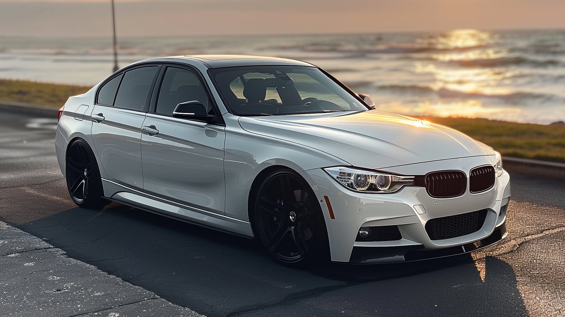 A white BMW 335i parked in front of the ocean.|a red car parked in a parking lot at sunset.