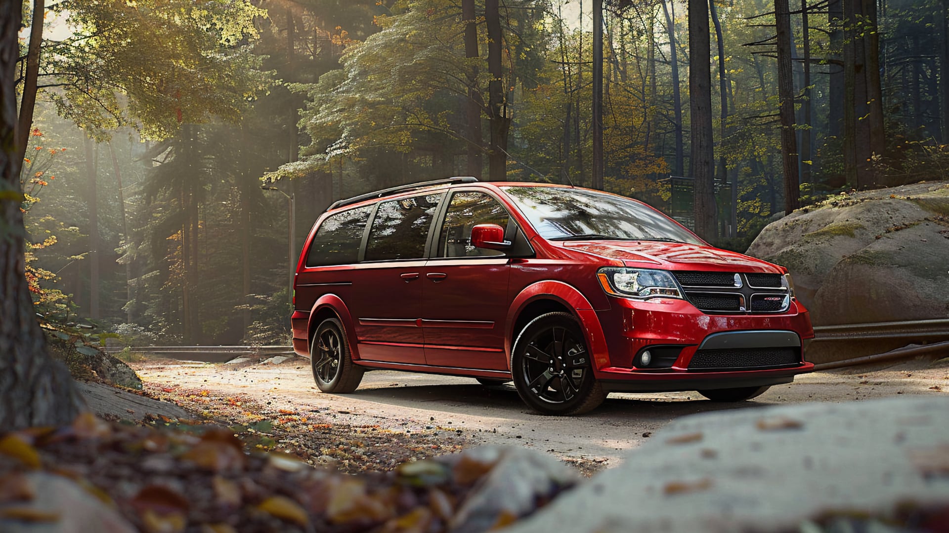 A red 2019 Dodge Grand Caravan parked in the woods.|a red van parked in a parking lot.