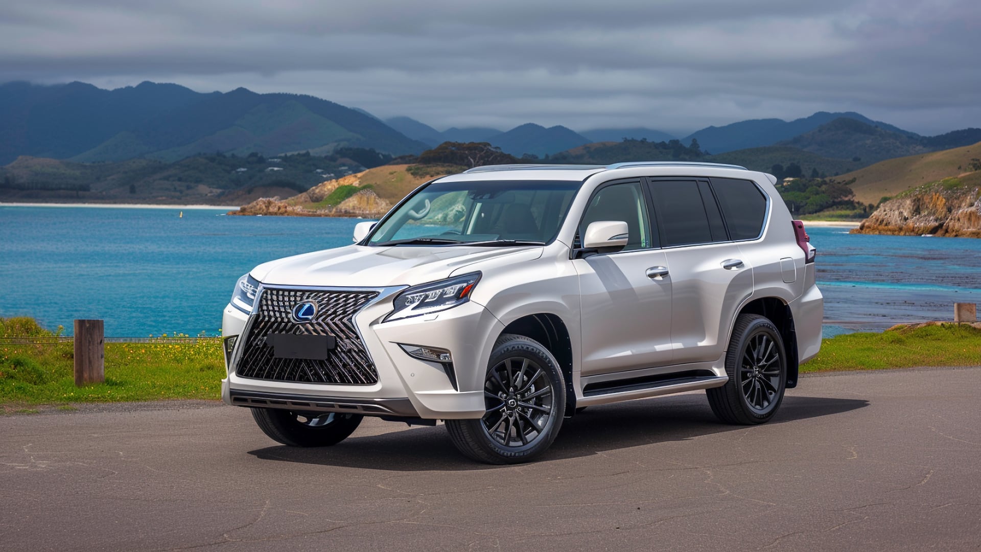The 2019 Lexus GX 460 is parked on a road near the ocean.|a silver suv parked in front of a building.