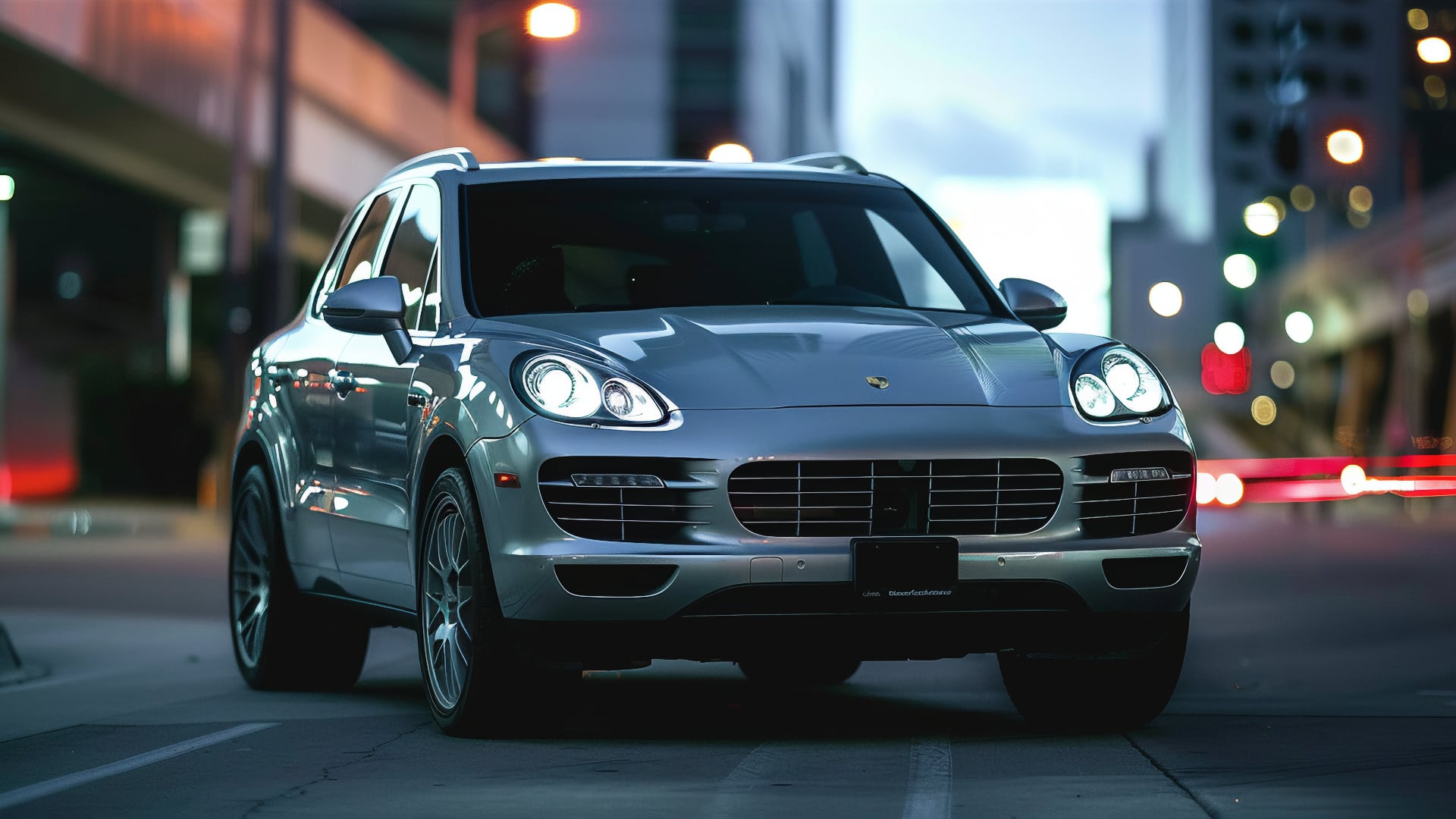 A silver Porsche Cayenne drives down a city street at night.|a silver porsche cayen is parked in a parking lot.