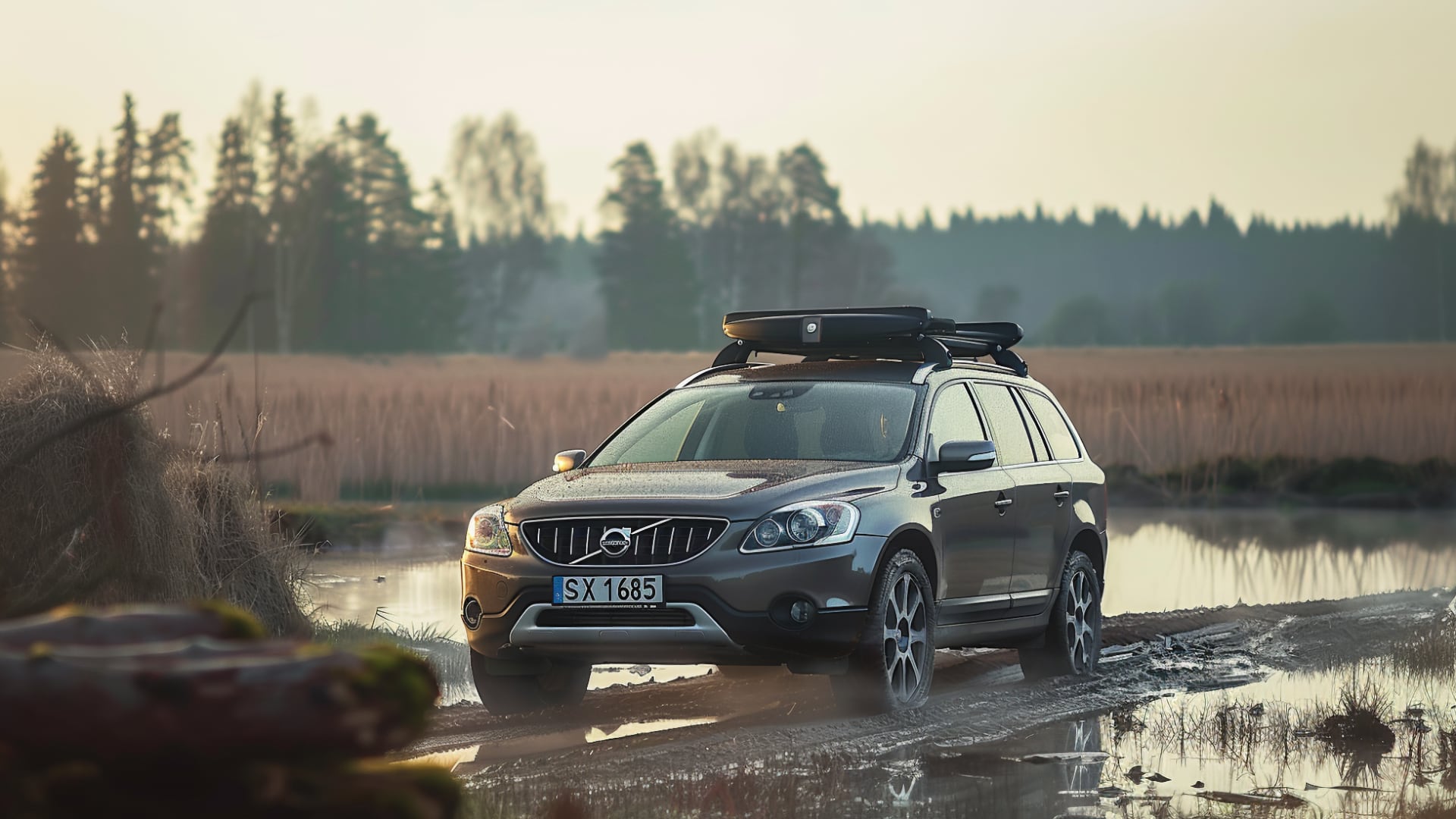 Volvo XC70 suv on a muddy road.|a couple of cars that are parked in the snow.
