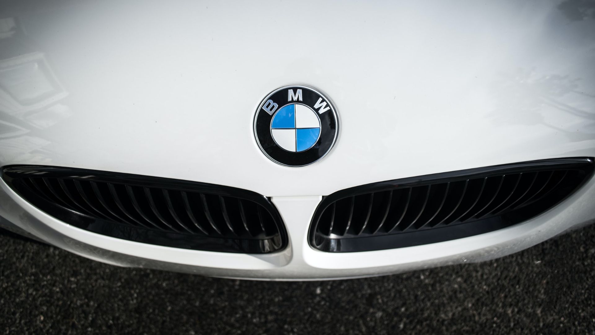 the front end of a white bmw car.|a silver car parked in front of a forest.|a close up of the tail lights of a car.