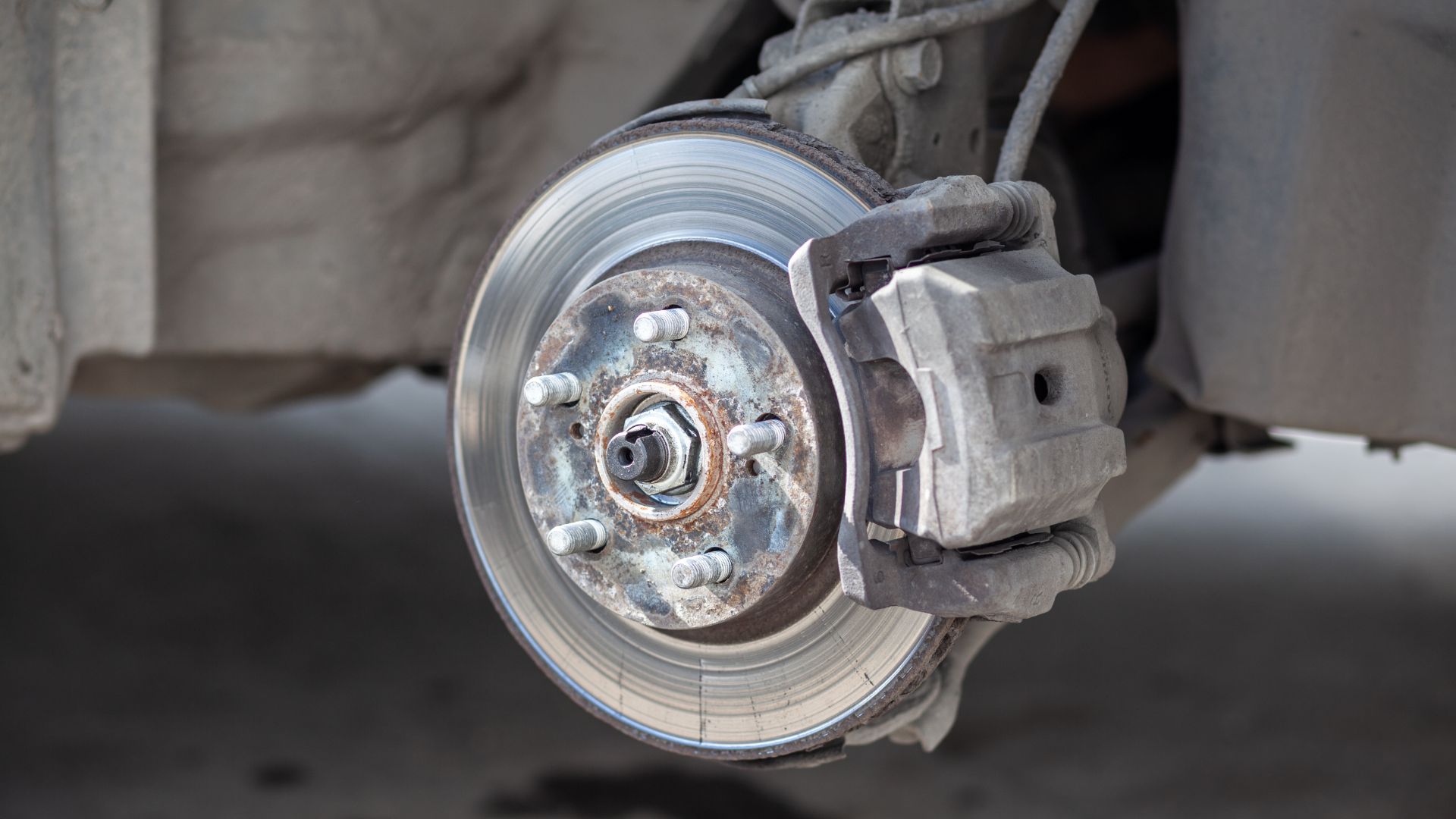 a close up of a brake on a vehicle.|a man working on a vehicle with a wrench.|a person holding money out of a car window.|a person working on a vehicle with a machine.|a man is working on a metal object.