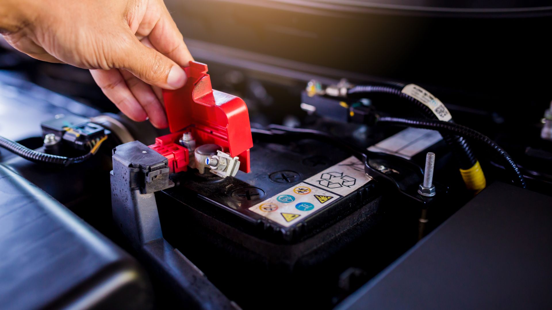 a person is working on a car battery.|two men working on a car engine in a garage.|a close up of a car's engine and gear.