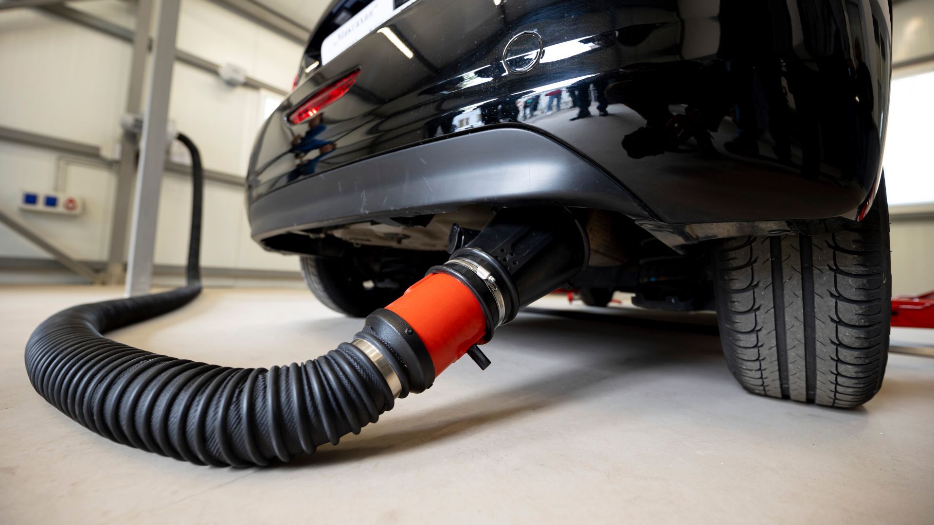 a car with a hose attached to it.|a man is using a hose to clean a car.