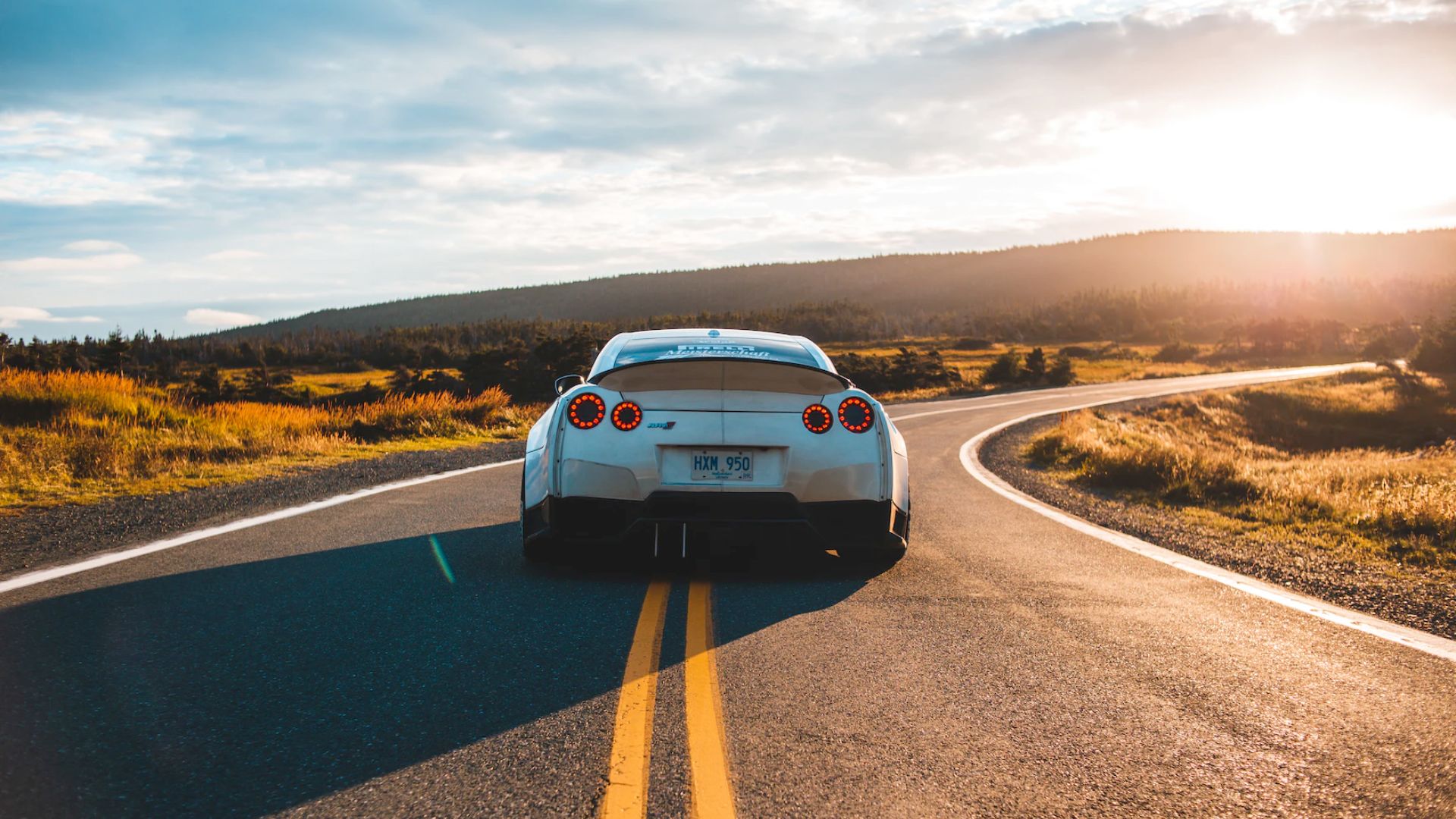 a white sports car driving down a country road.|a person wearing gloves holding a small object.|a close up of a car's front suspension.|a close up of a red and black shock spring.