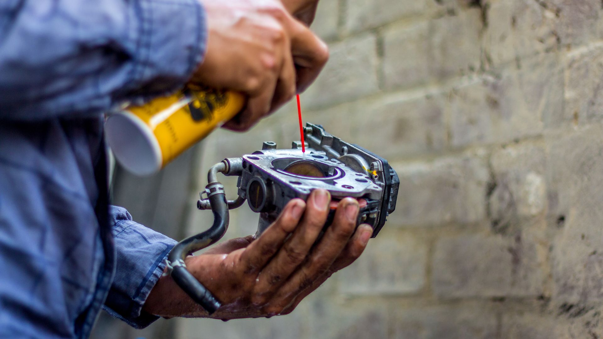 a man holding a small engine in his hands.|a person sprays a brake with a sprayer.