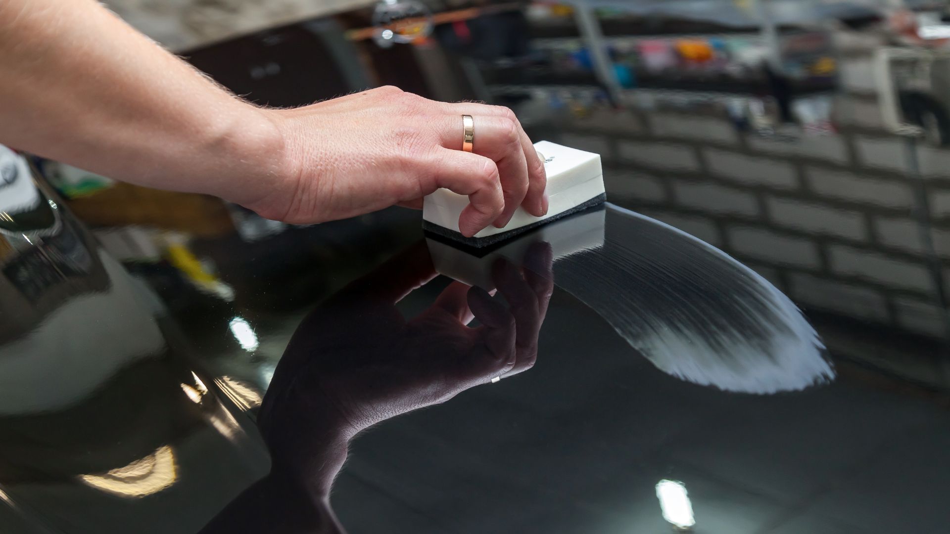 a person's hand on top of a glass table.|a man waxing a car in a garage.|a person wiping down a red car with a cloth.|a man polishing the hood of a car.
