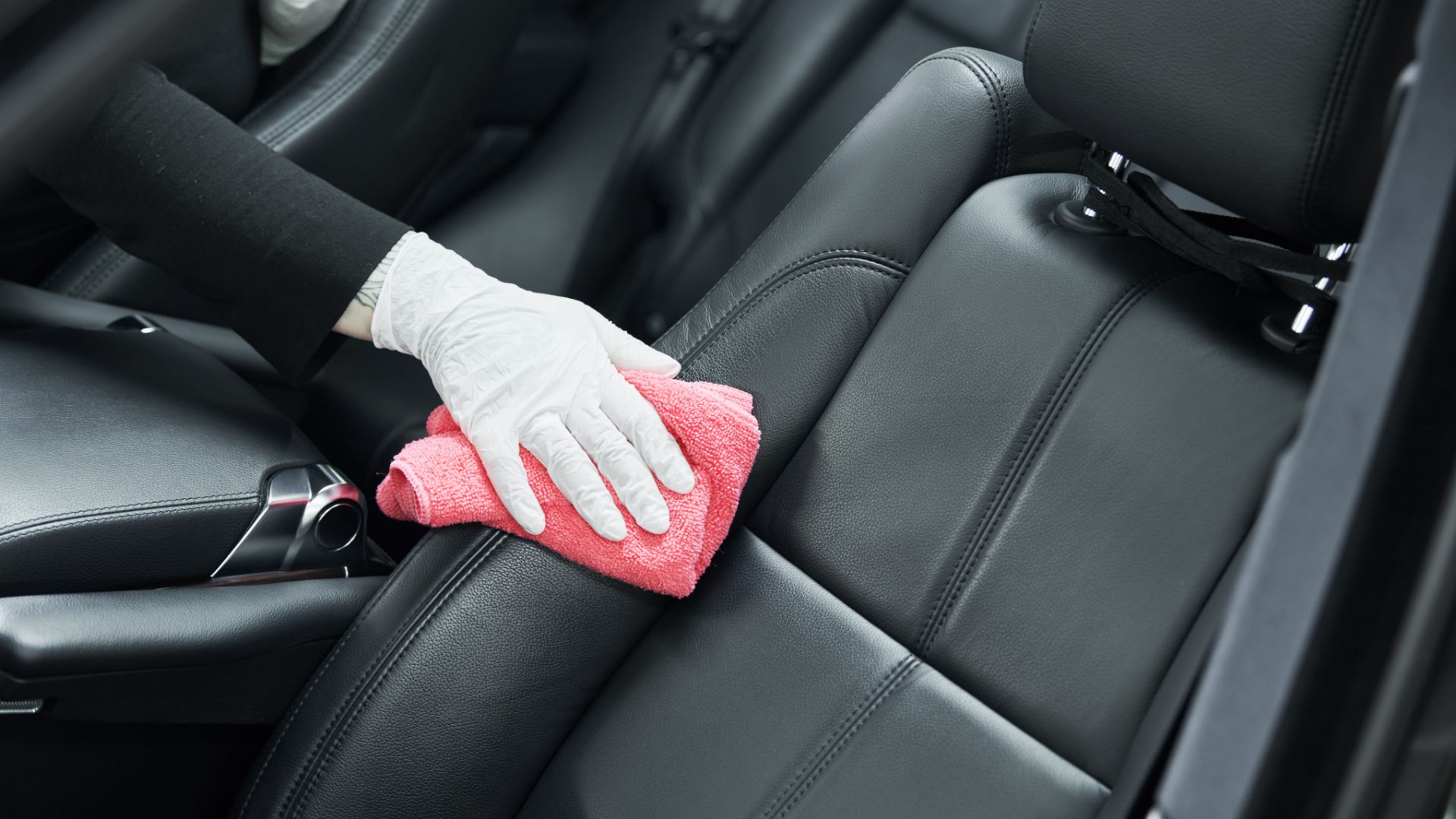 a person cleaning a car with a micro cloth.|a person in blue gloves is cleaning a car seat.|a person cleaning a car seat with a cloth.
