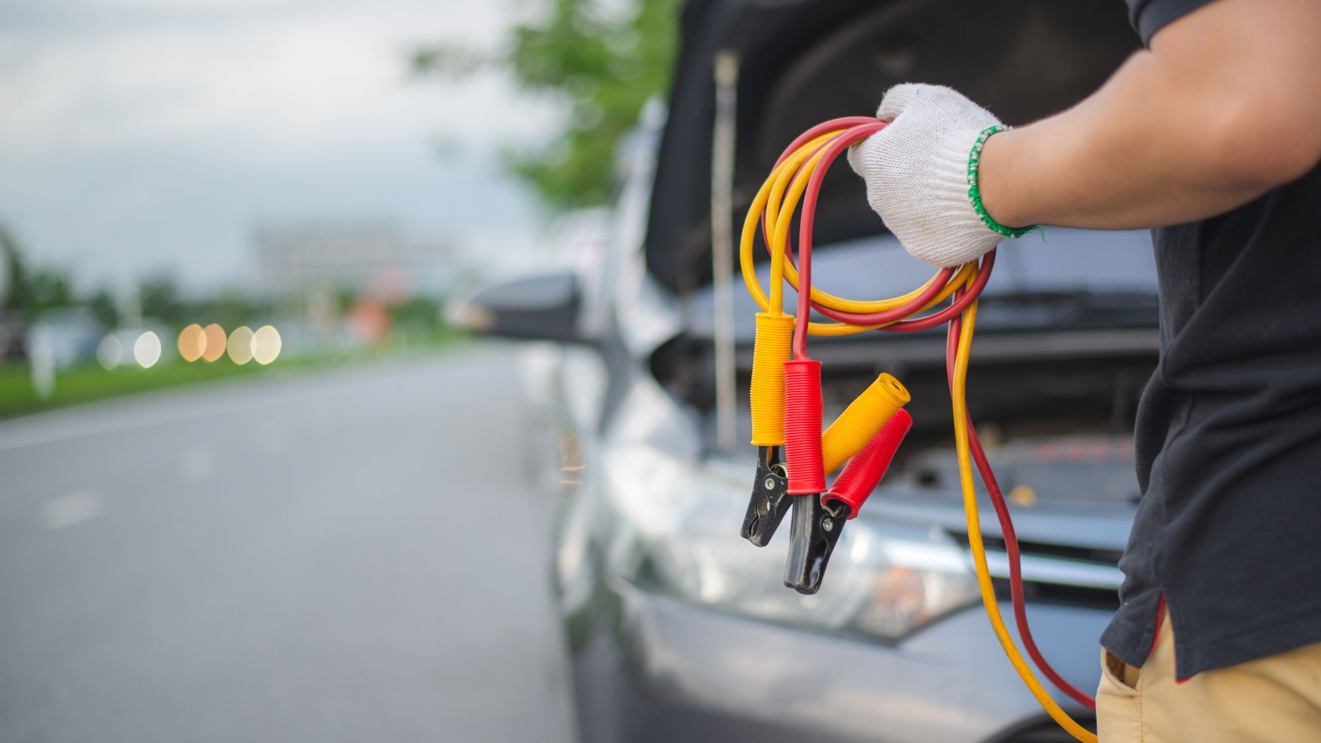 a man is holding a jump rope in front of a car.|a couple of cars parked next to each other in the snow.