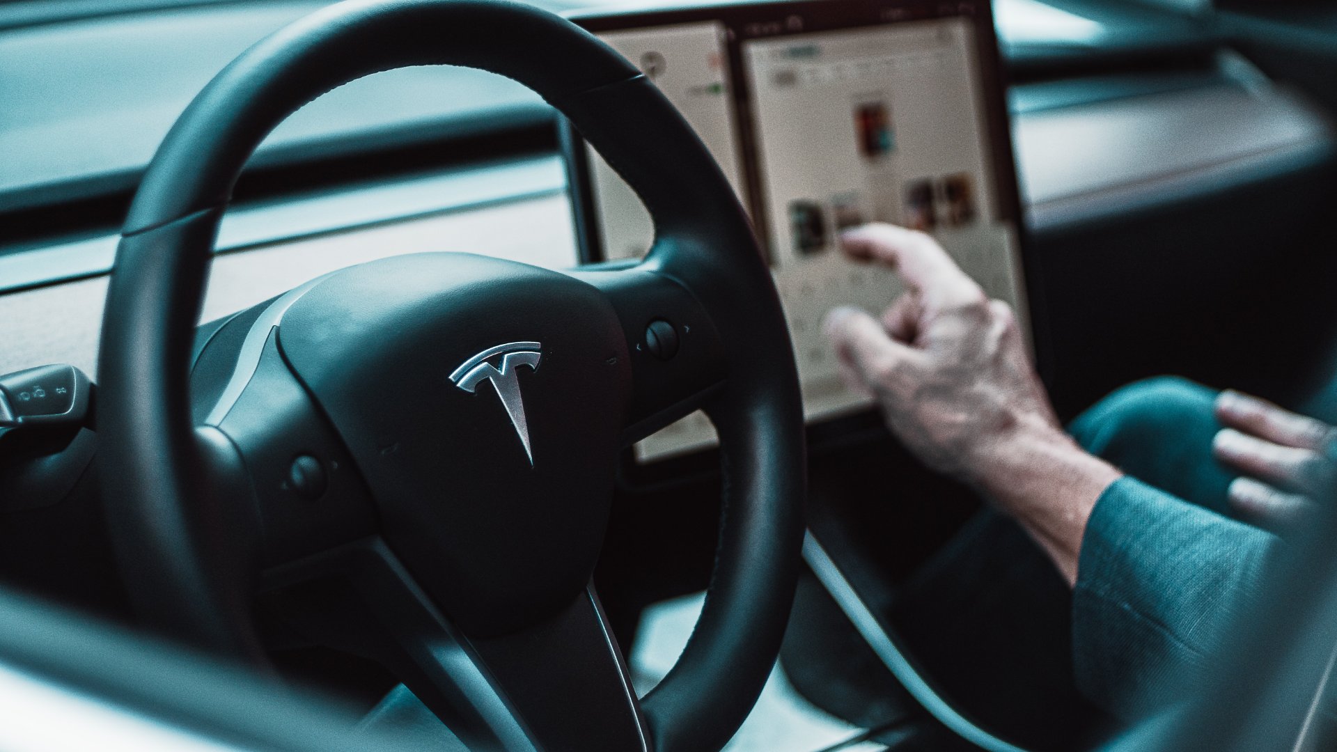 a person using a tablet in a car.|a black car is parked in a parking lot.