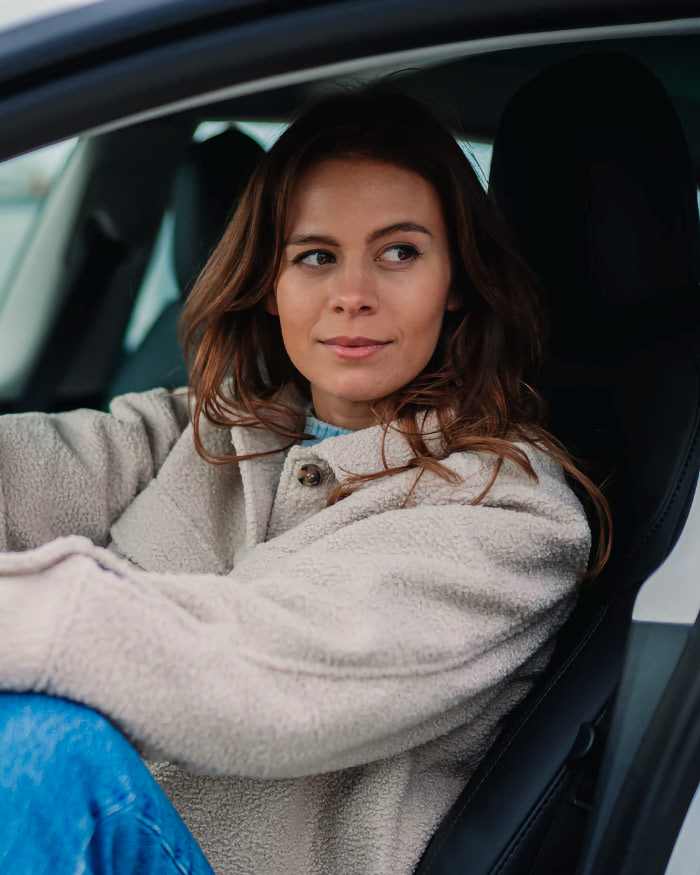A woman sitting in a car with her hand on the steering wheel.