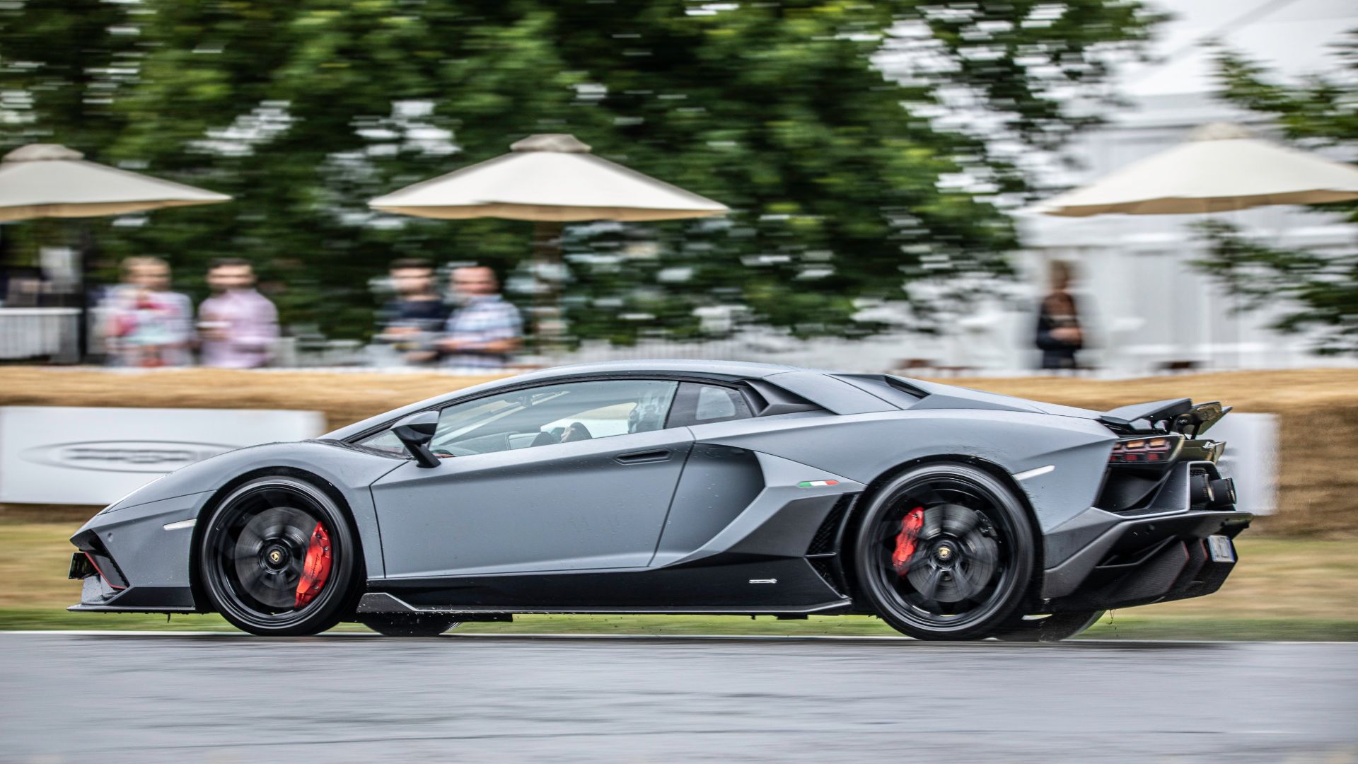 a grey sports car driving down a race track.|a yellow sports car driving on a race track.