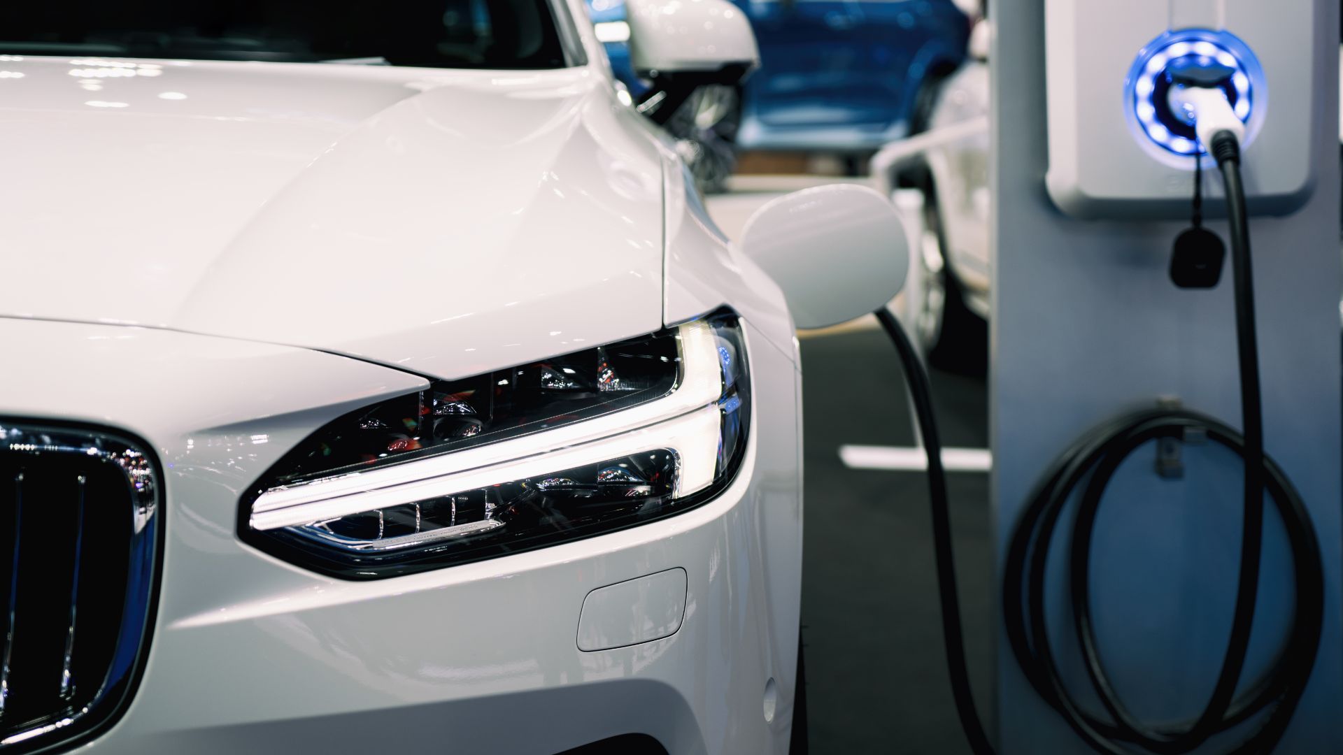 a person pumping gas into a car at a gas station.|a parking lot filled with lots of white cars.|an electric car plugged in to a charging station.|two women standing next to a car at a charging station.