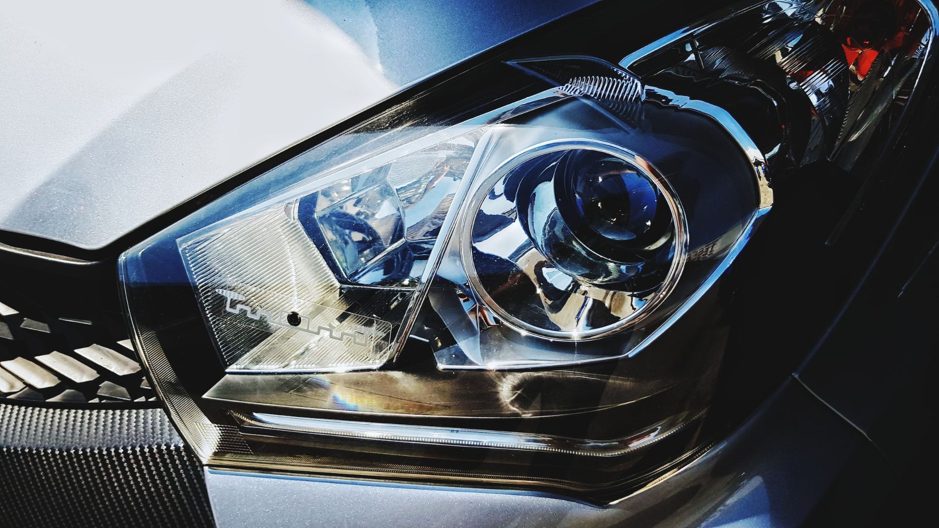 a close up of a headlight on a car.|a close up of a blue button on a car dashboard.|a close up of a person holding a camera.