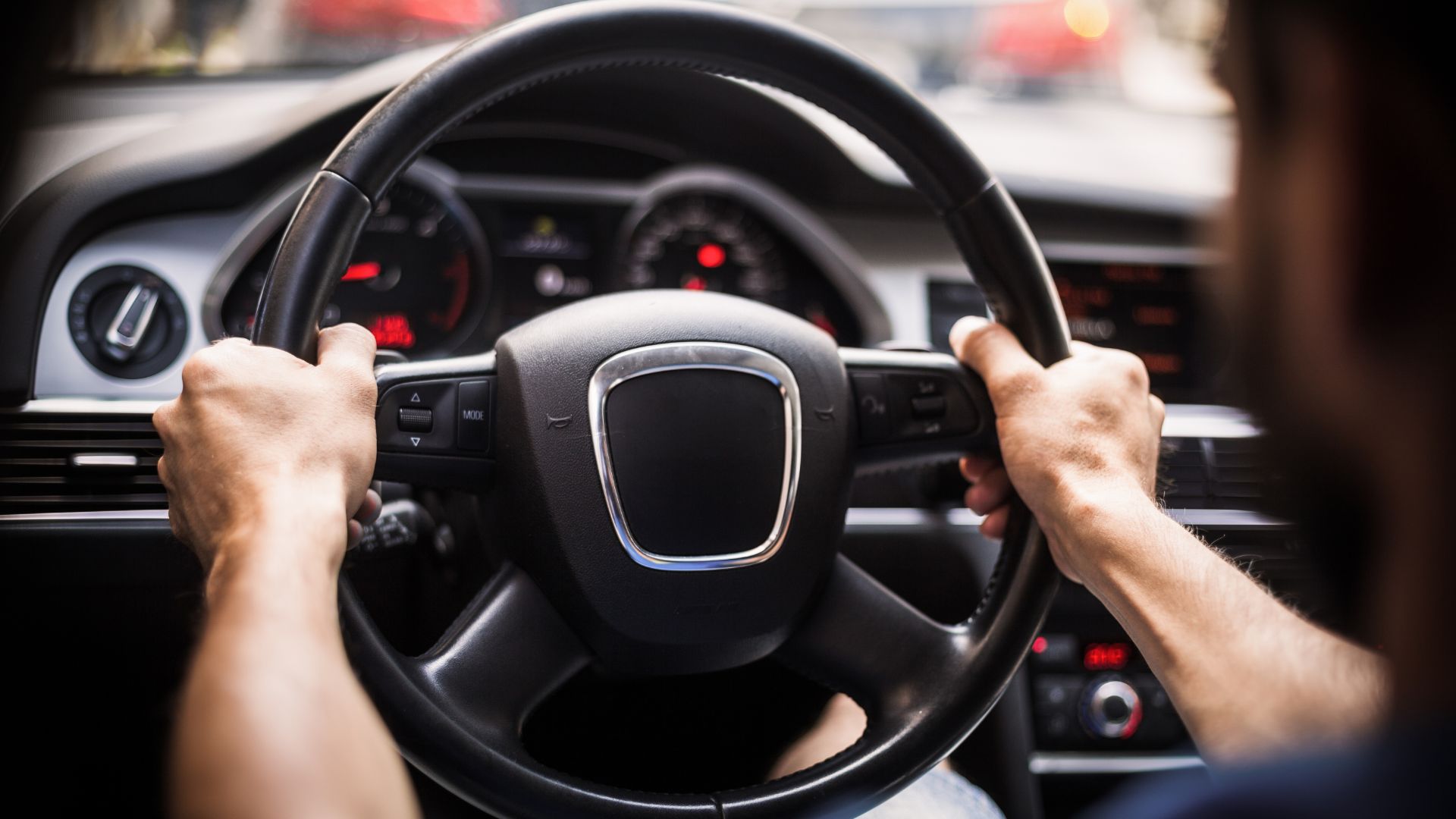 a man driving a car with a steering wheel.|a white car on a lift in a garage.