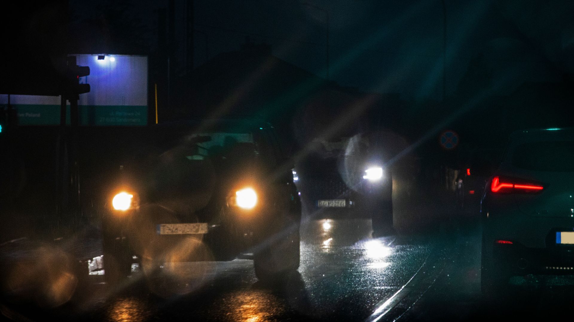 a couple of cars driving down a street at night.|a close up of a car mirror with trees in the background.