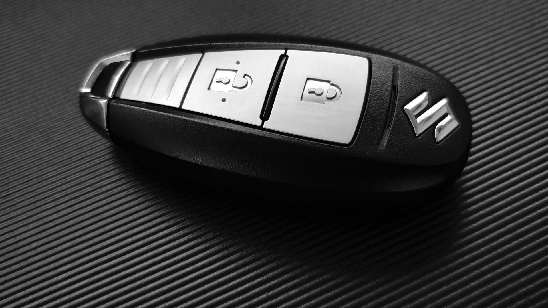 a close up of a remote control on a table.|a hand holding a cell phone in front of a white car.
