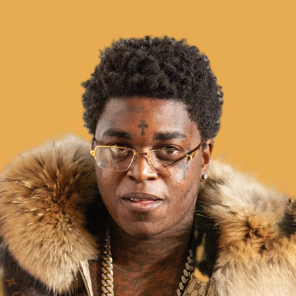 a man wearing glasses and a fur coat.|a blue car parked on the side of the road.