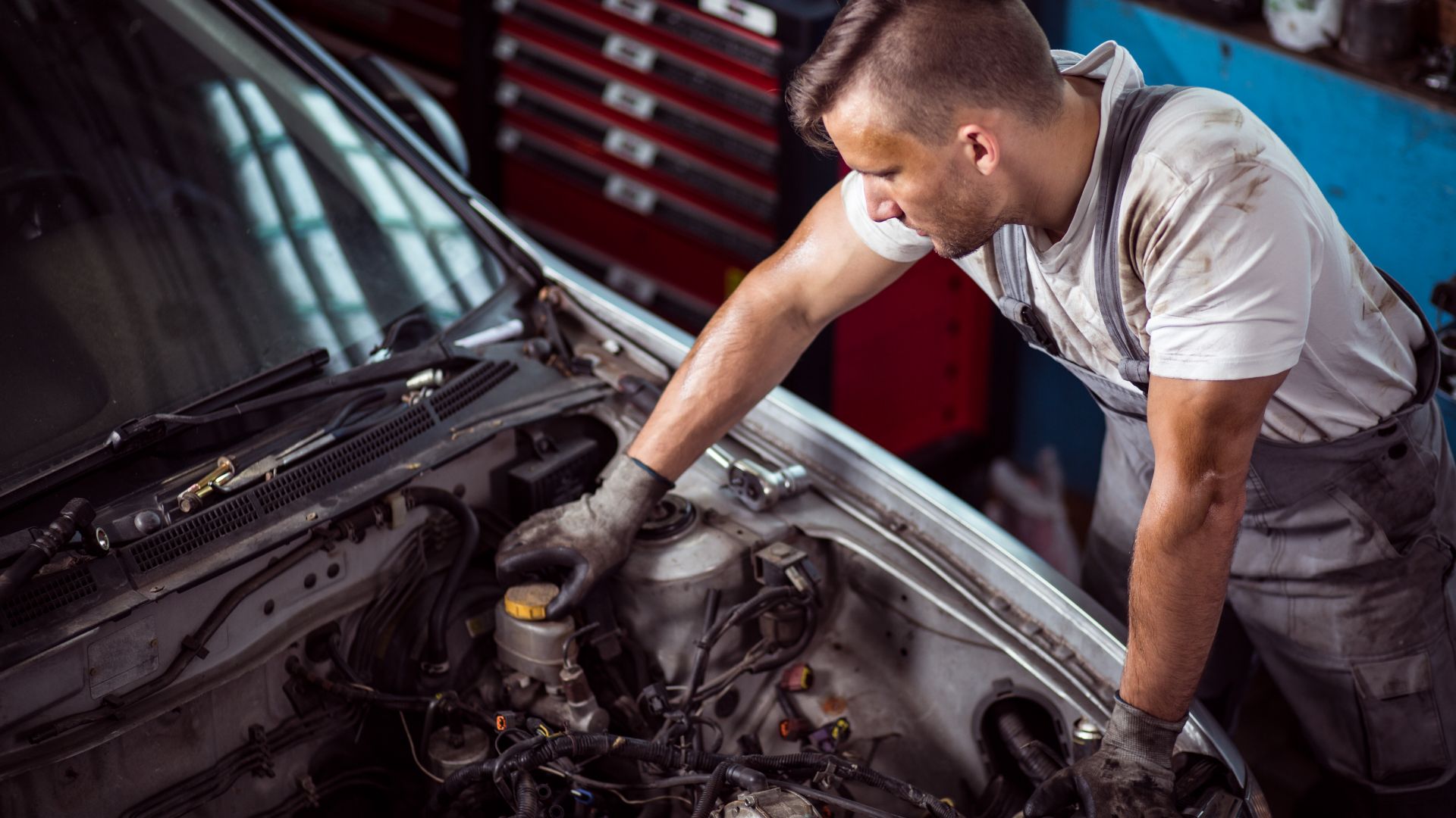 a man working on a car engine in a garage.|a person in gloves is pouring a motor oil into a car.|a man is working on a car engine.|a close up of a car's engine and oil can.