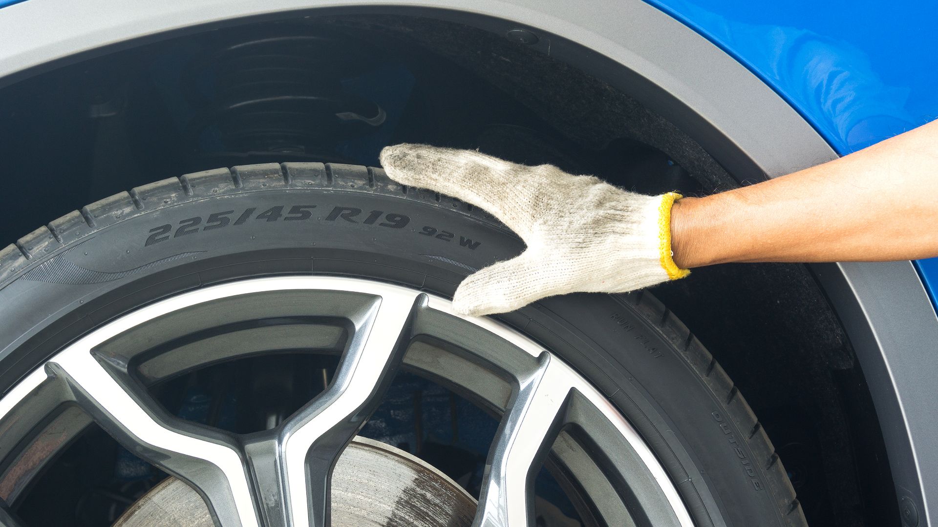 a person with a glove cleaning a car tire.|a man is cleaning a tire with a cloth.