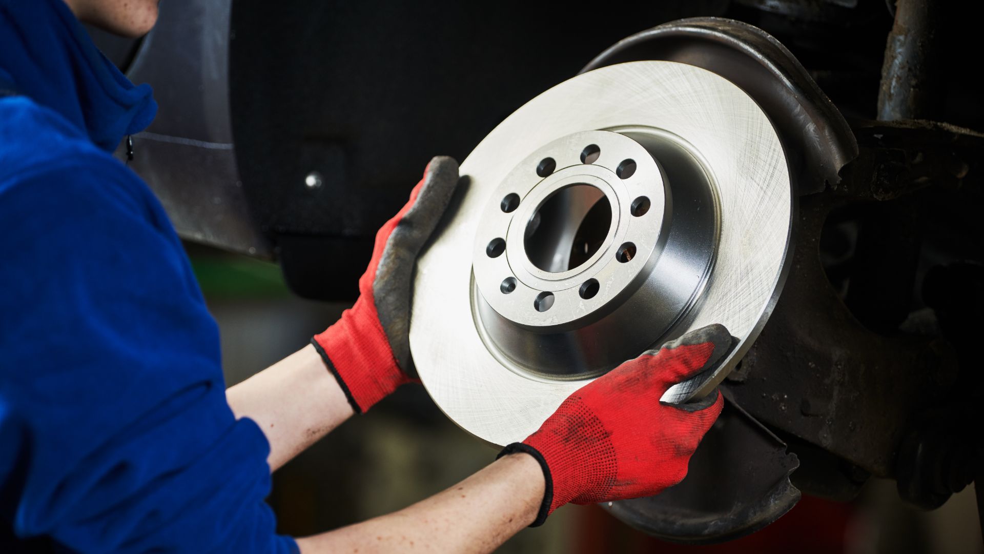 a woman is working on a brake assembly.|a man working on a brake assembly on a vehicle.|a person's feet in a car with a brown shoelace.|a close up of a person's shoes on a vehicle.