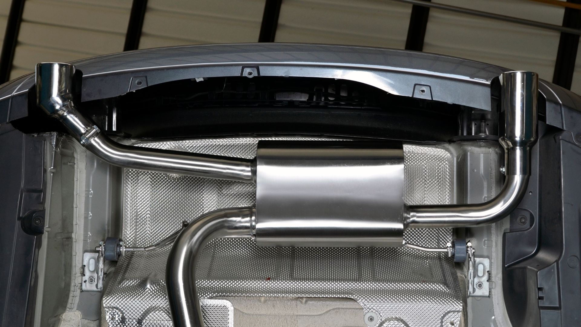 a close up of a metal object in a garage.|a close up of a exhaust pipe on a vehicle.|a close up of a metal pipe with a green wall in the background.