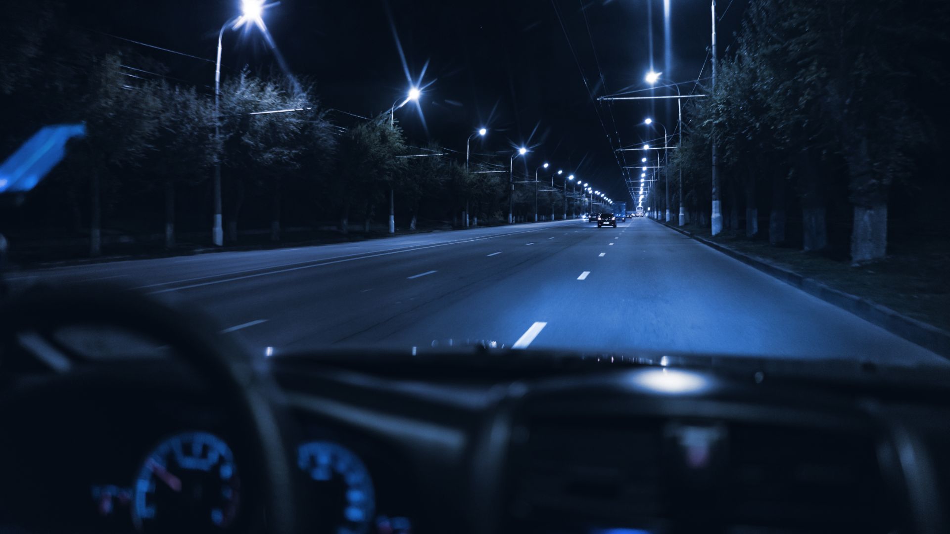 a car driving down a street at night.|a car driving down a street at night.|a man driving a car with his hands on the steering wheel.|a dark road at night with a herd of deer on the side.|a couple of cars driving down a street at night.