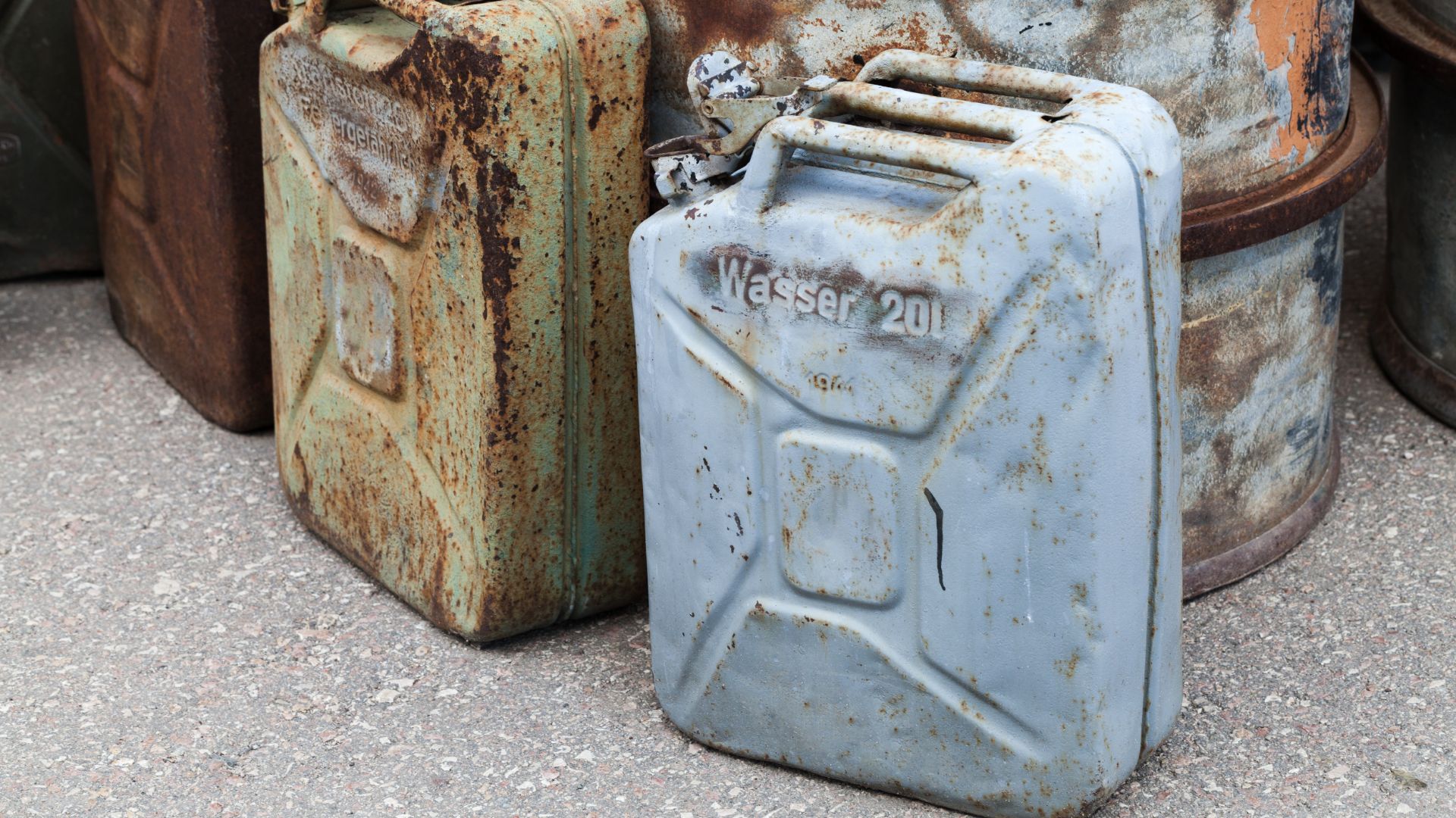 a group of rusty gas cans sitting next to each other.|a sign on a chain link fence that says hazardous waste.