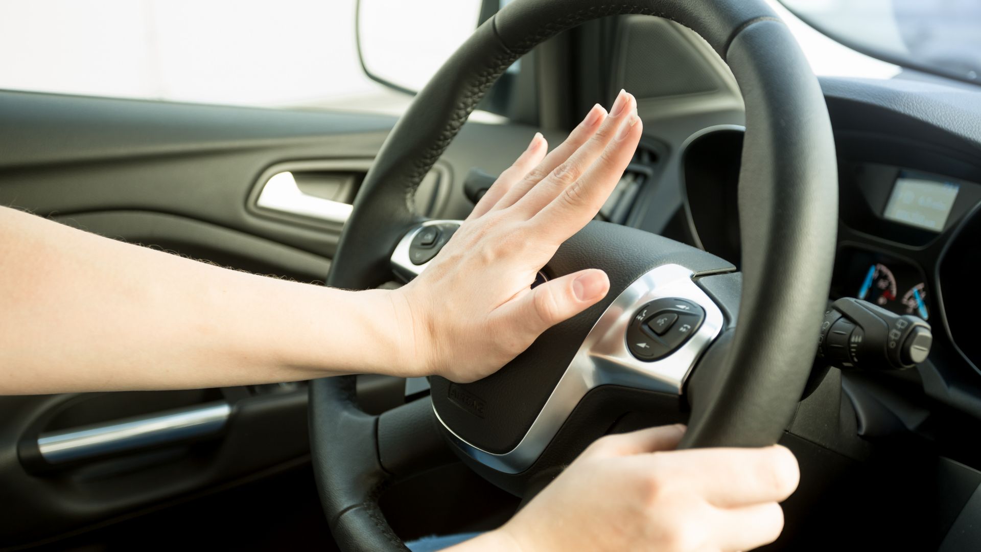 a person driving a car with their hands on the steering wheel.|a woman driving a car with her hand on the steering wheel.|a close up of a steering wheel and dashboard of a car.|a close up of a leather surface with a small metal object on top of it.