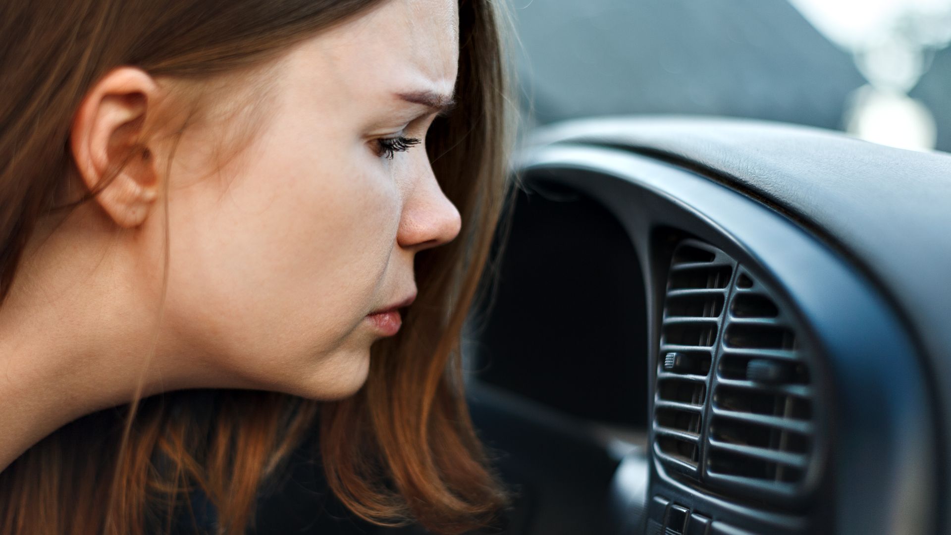 a woman looking at the air conditioner in her car.|a person in blue gloves holding a piece of paper.