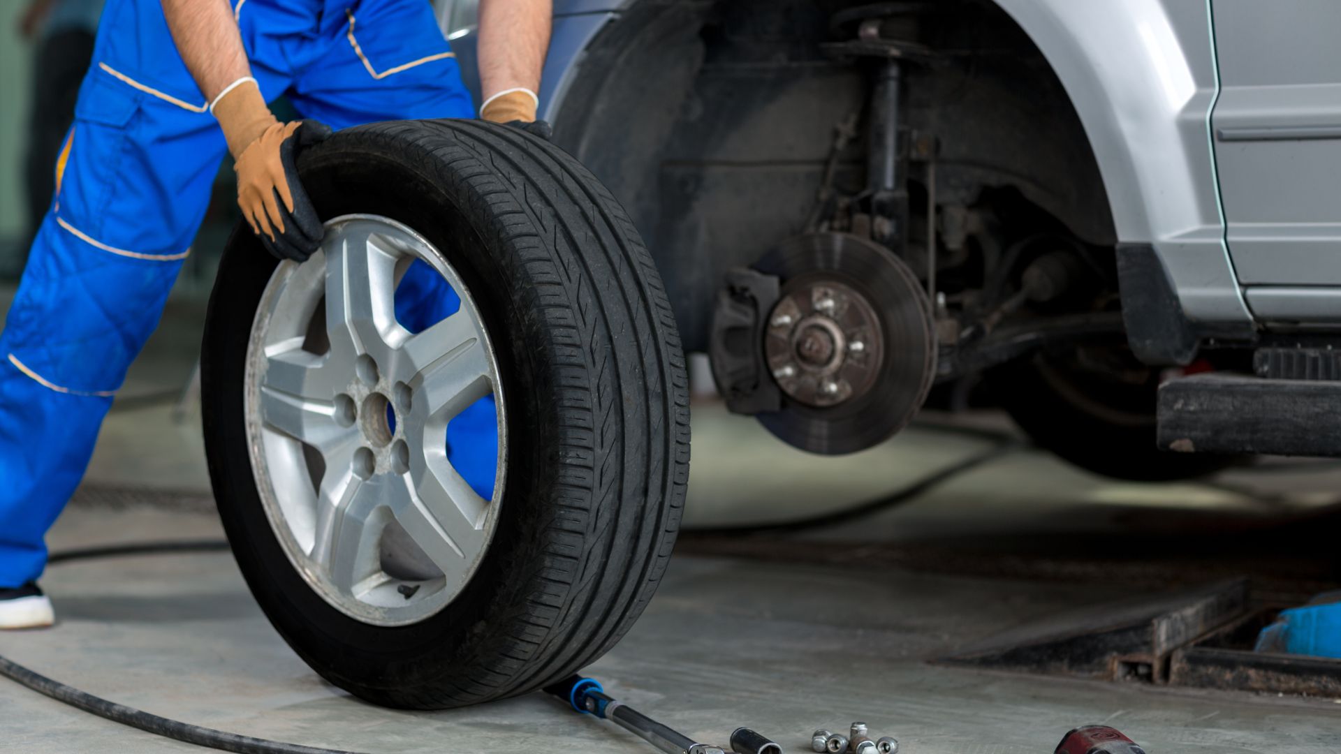 a man working on a tire in a garage.|a person changing a tire with a wrench.|a car is parked on the side of the road.|a man holding a red triangle sign next to a car.