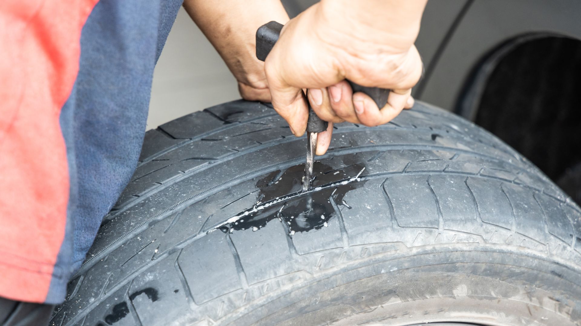 a person is holding a wrench on a tire.|a set of tools are laying on the ground next to a tire.|a person working on a tire on a machine.