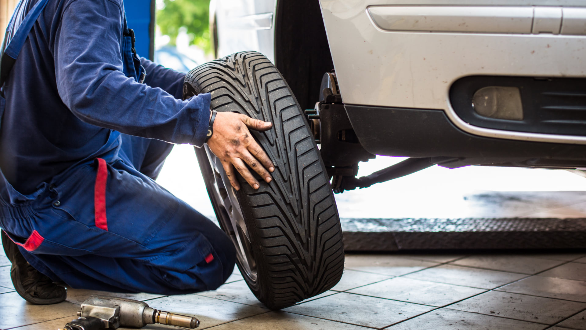 a man working on a tire with a wrench.|a man working on a motorcycle in a garage.