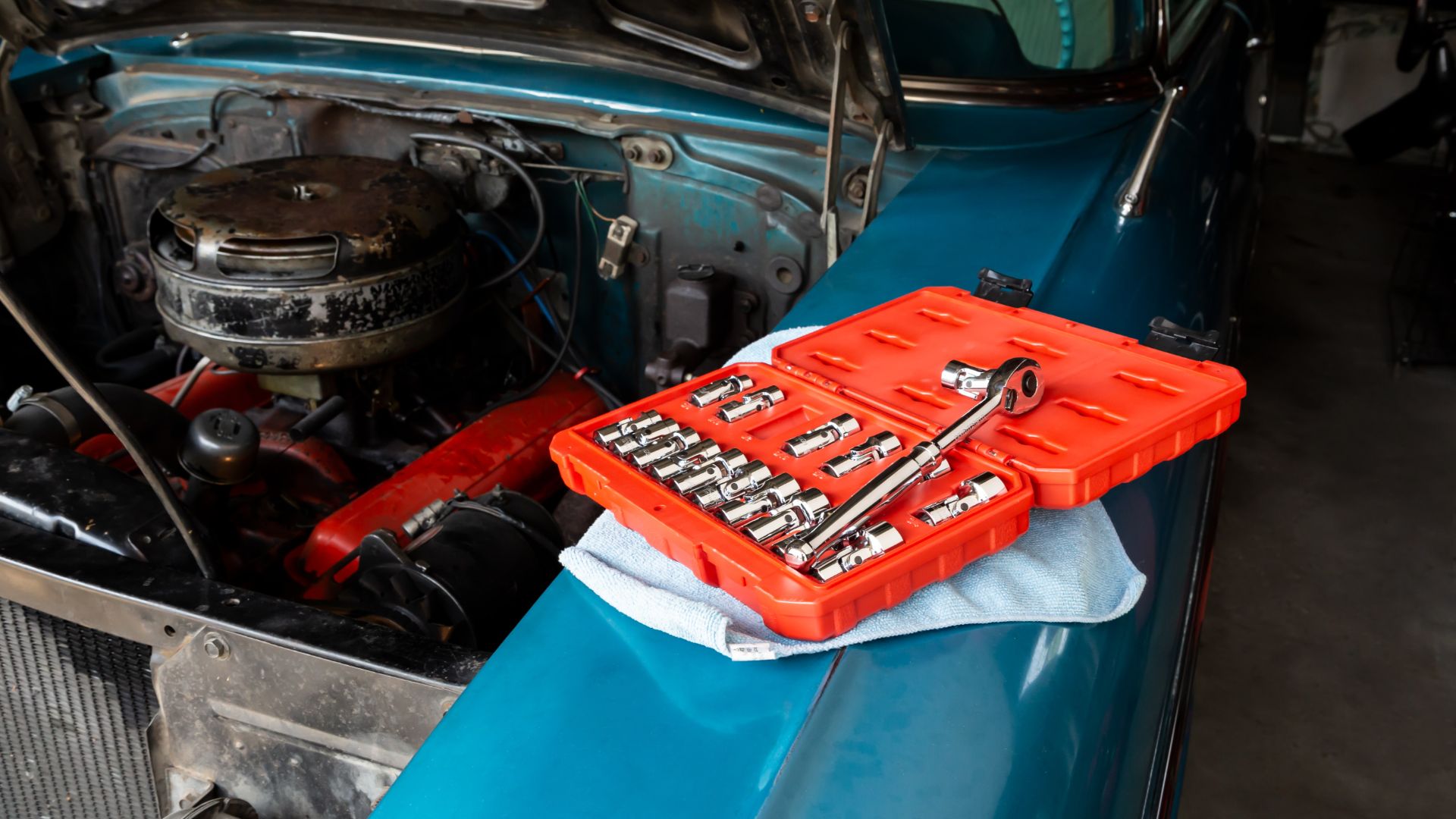 a wrench sitting on top of a tool box in front of a car.|a person holding a pair of scissors in their hand.