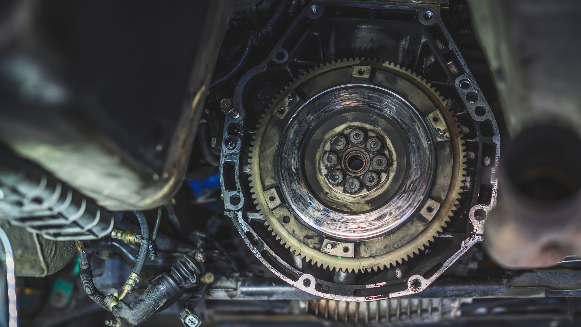 a close up of a metal gear on a vehicle.|a car being worked on in a garage.|a close up of a metal object with a wrench.|a close up of a car engine with wires.|the engine compartment of a vehicle with the top part of the engine exposed.