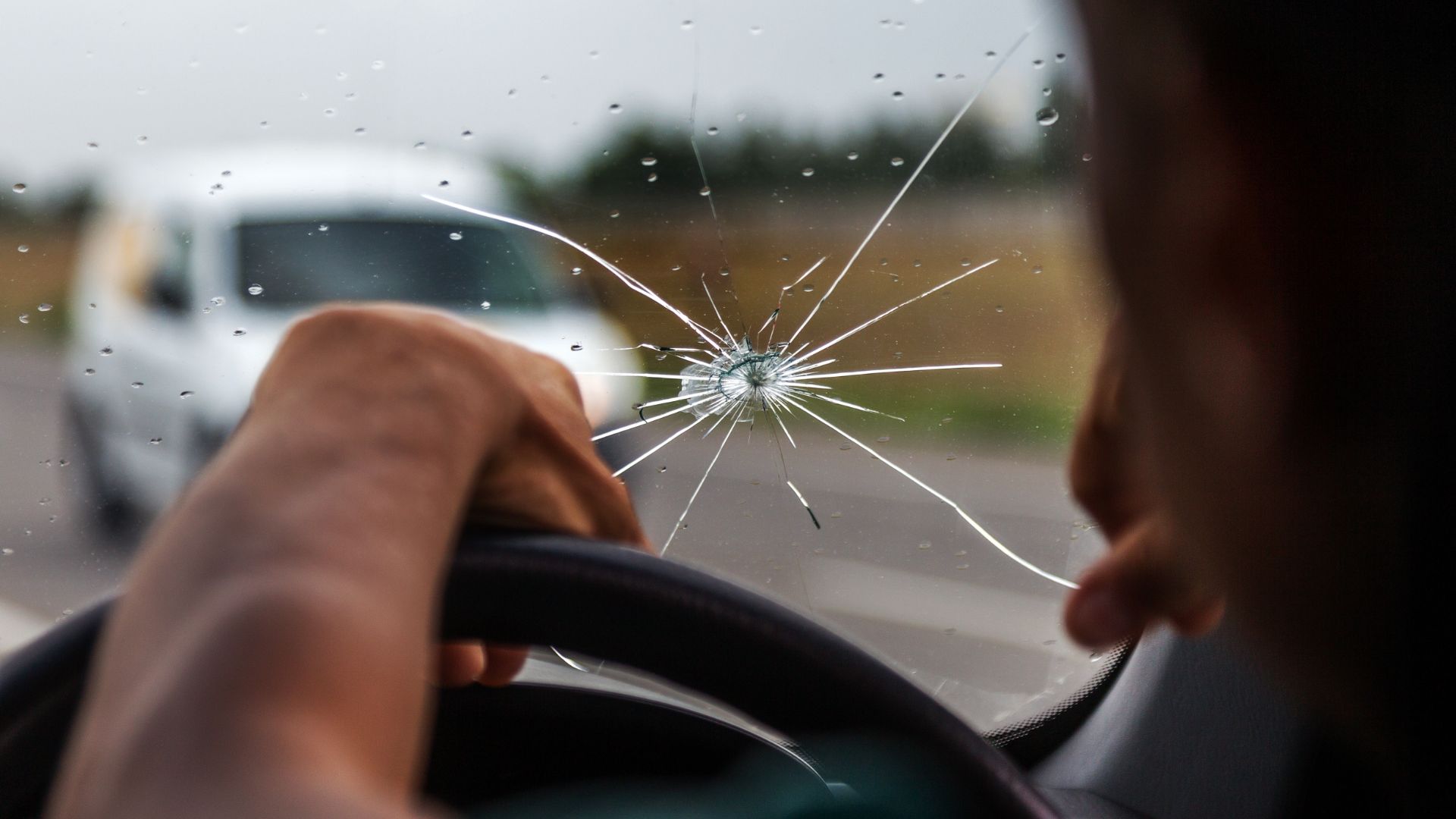 a person holding the steering wheel of a car with a broken windshield.|a person is holding a camera on a tripod.